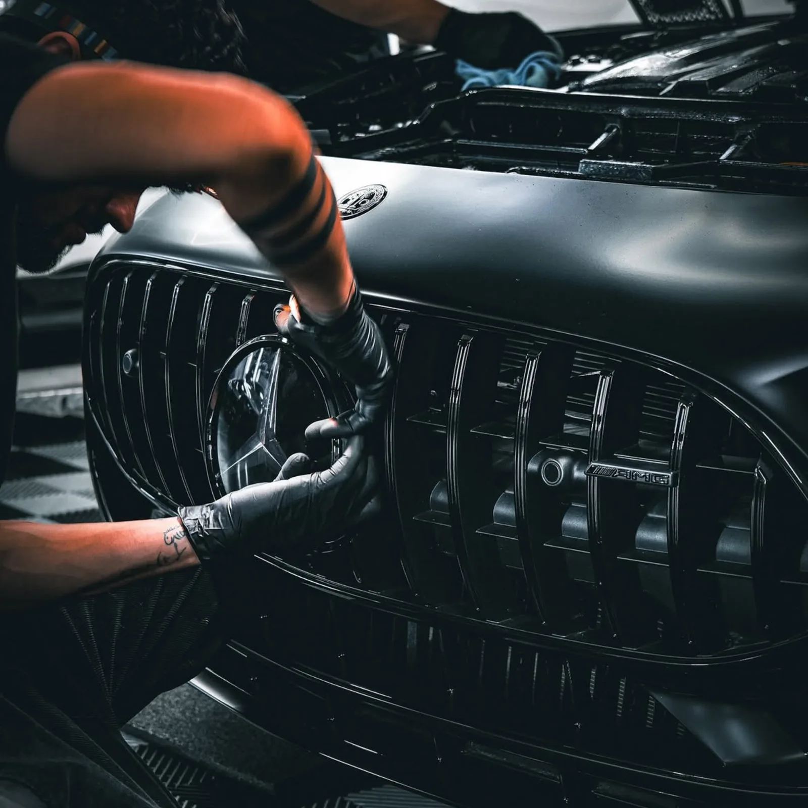 Gloved hands refitting the badge on the blacked out grille of a Mercedes-AMG