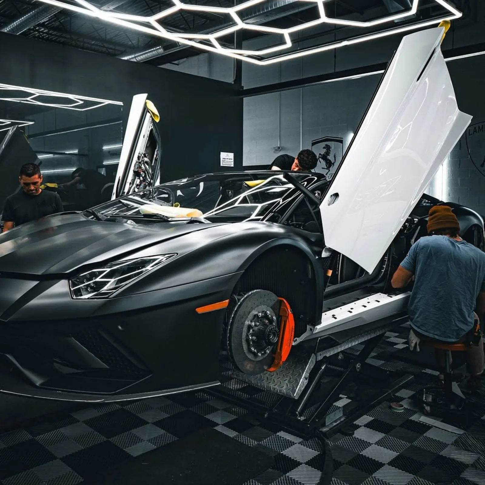 Matte black Lamborghini Aventador under hexagon lighting with its doors raised and brakes exposed