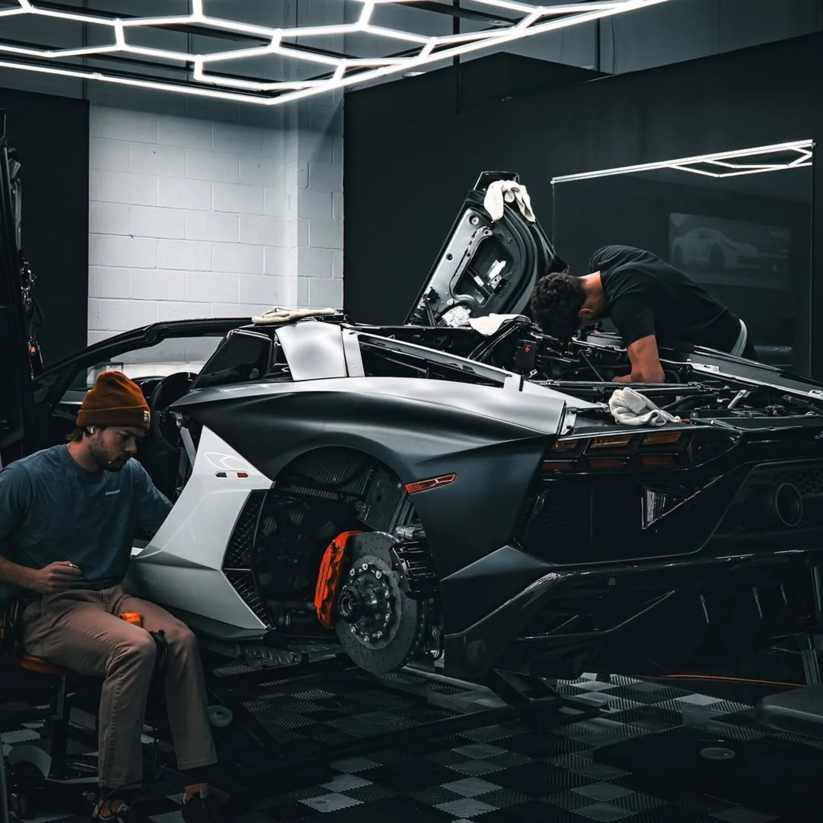 Lamborghini Aventador roadster partly disassembled in a lit studio bay, panels off and engine cover raised